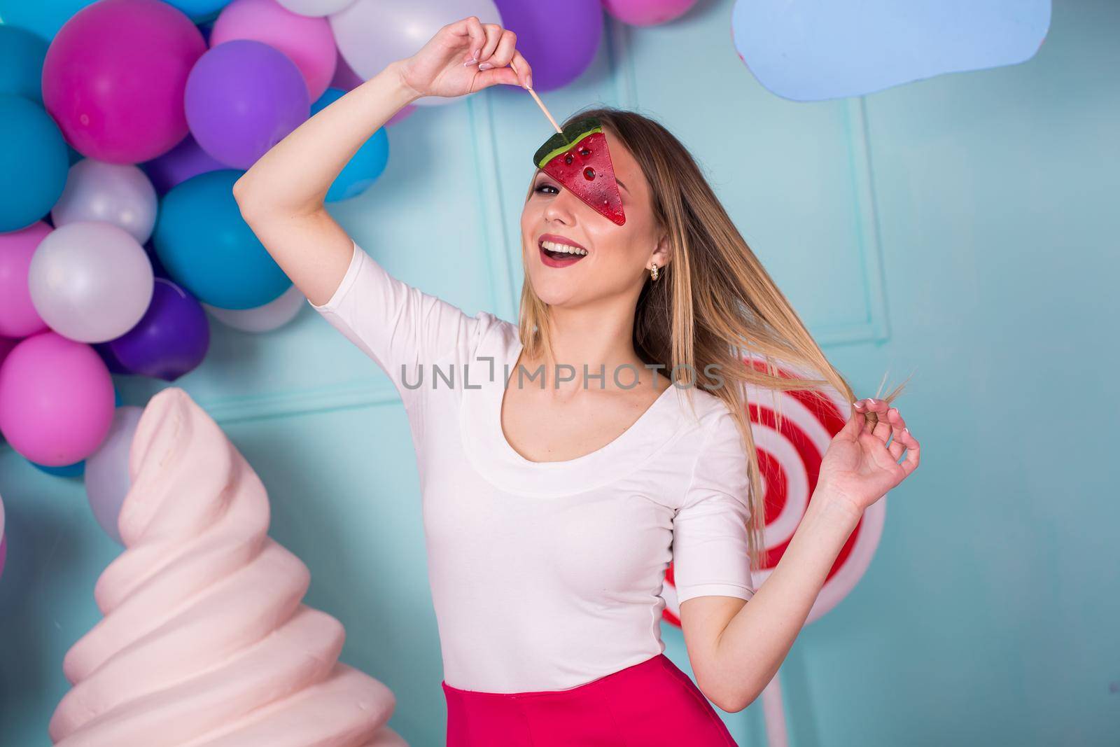 Portrait of amazing sweet-tooth woman in pink dress holding candies and posing on background decorated with huge ice cream. Lollipop watermelon. by StudioPeace