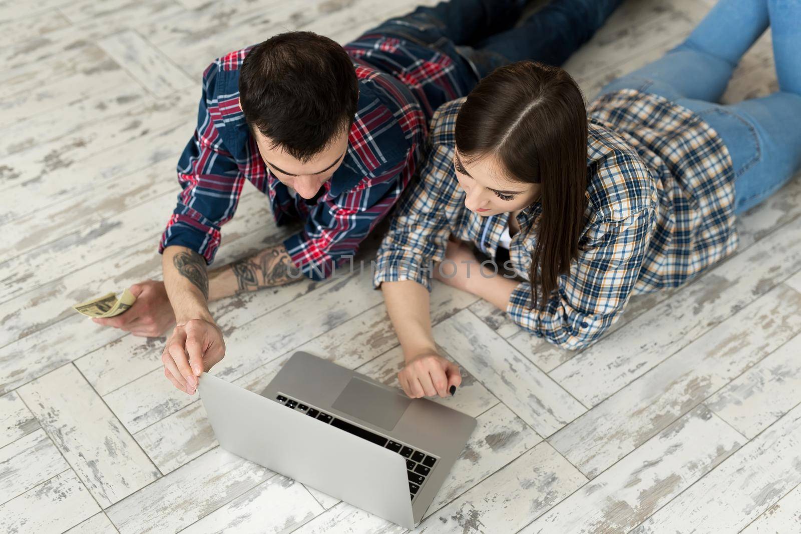 Portrait of a cute young couple lying on the floor at home and managing budget using laptop