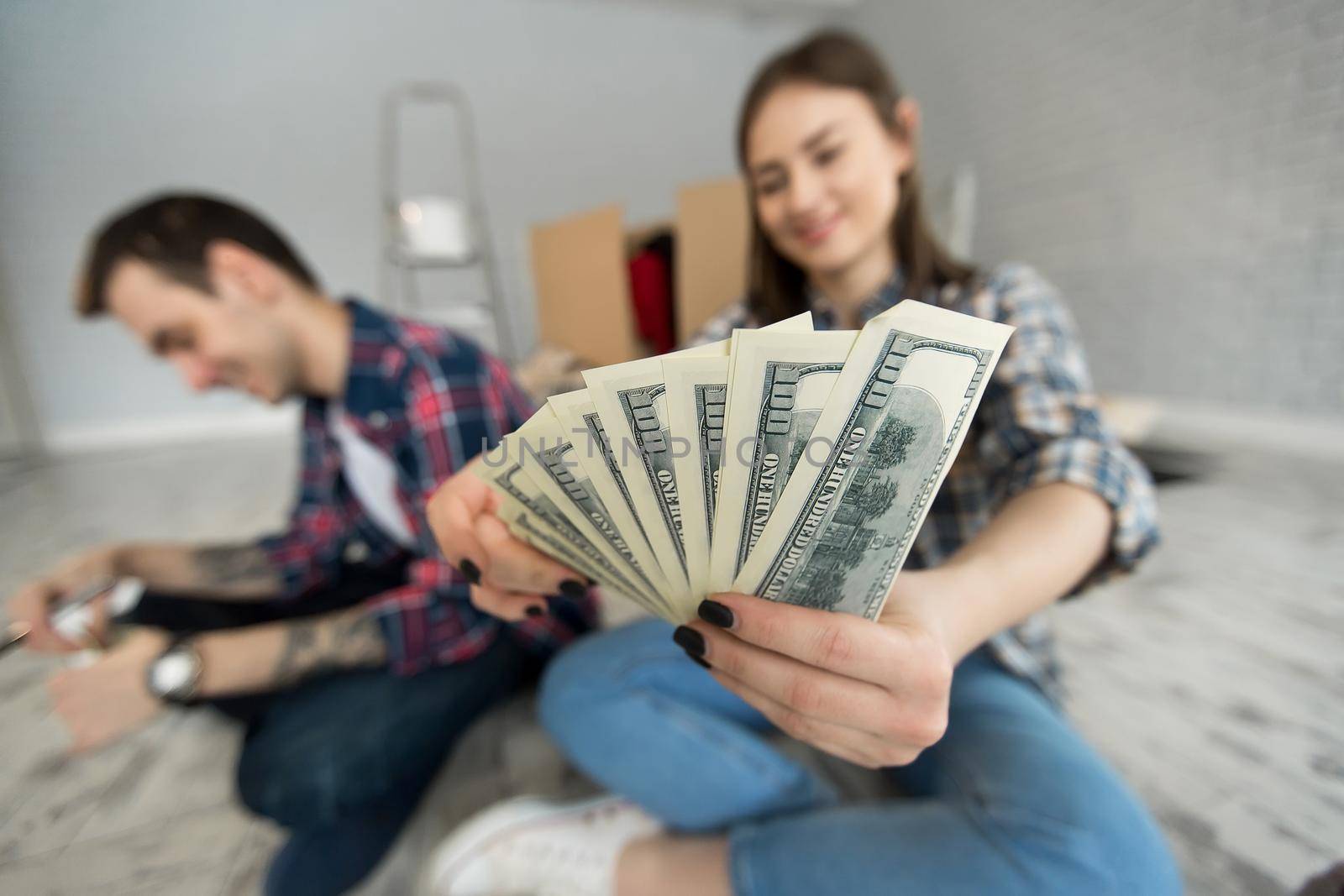 Young couple counting money while sitting on floor in new apartment. by StudioPeace