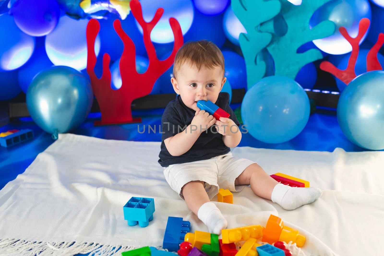 Small boy in a smart suit sits on the floor and plays with a construction kit by StudioPeace