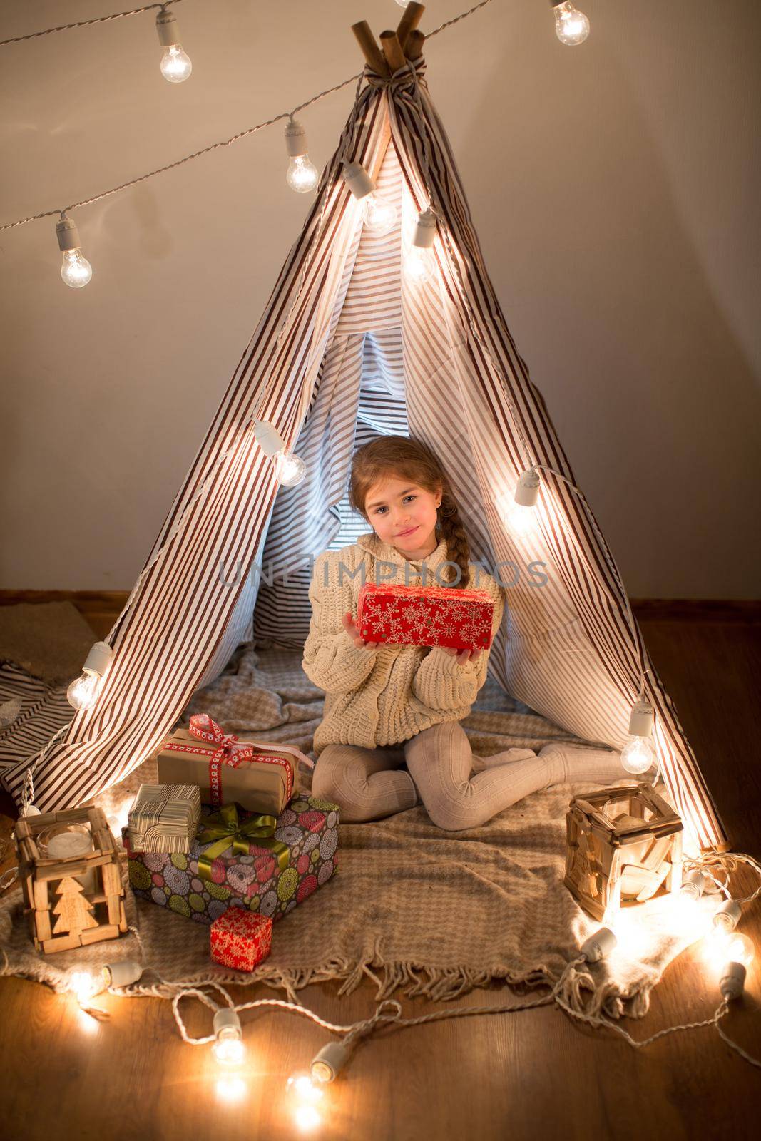 Beautiful little girl sitting with a present in his hands. Deploy Christmas gift box on holiday in the evening in the beautiful interior room. New year. Studio. by StudioPeace