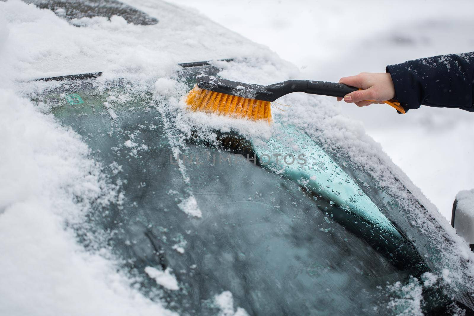 A woman removes snow from the windshield of a car