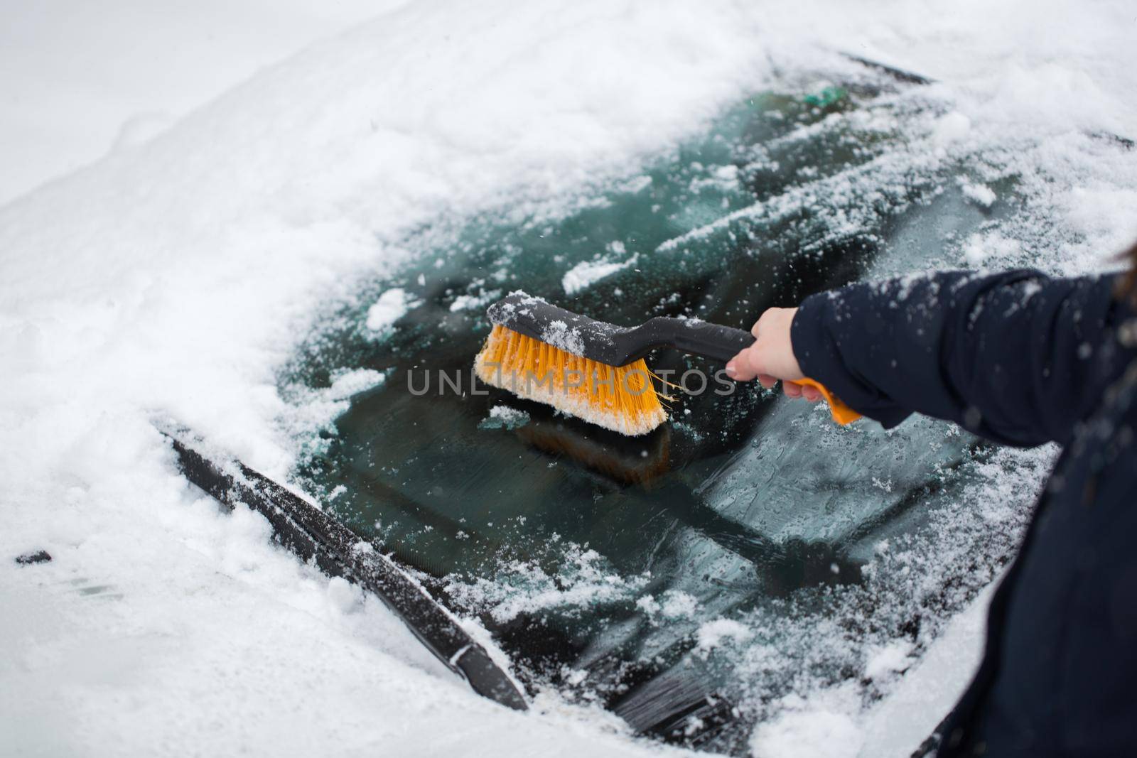 A woman removes snow from the windshield of a car