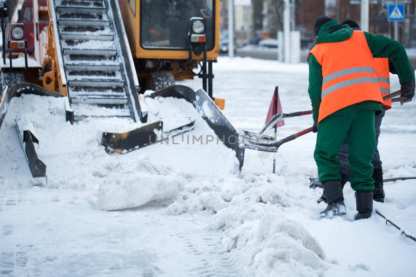 Tractor cleaning the road from the snow. Excavator cleans the streets of large amounts of snow in city. Workers sweep snow from road in winter, Cleaning road from snow storm by StudioPeace