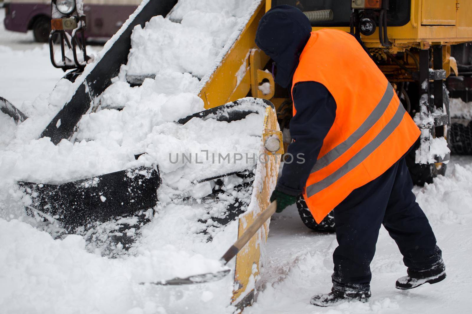 Claw loader vehicle removes snow from the road. Employees of municipal services helps shovel snow into a snowplow by StudioPeace