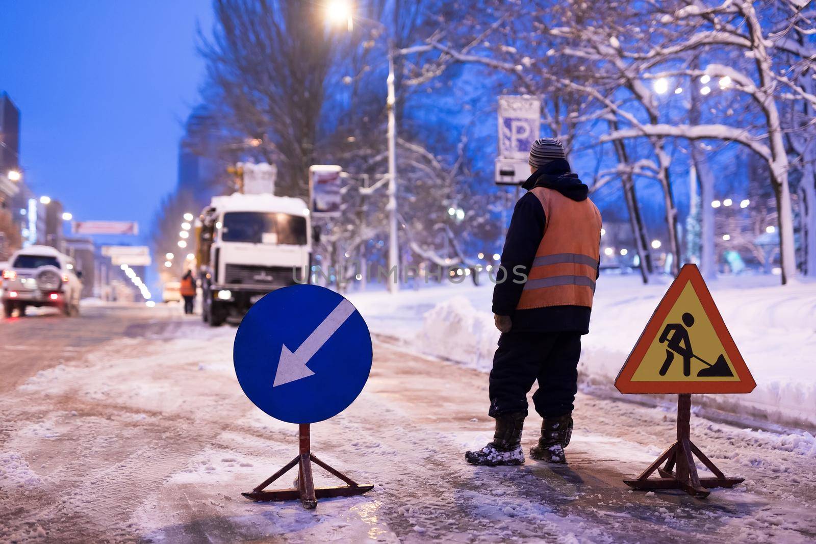 Snowplow removes snow from a city street. Warning road sign.