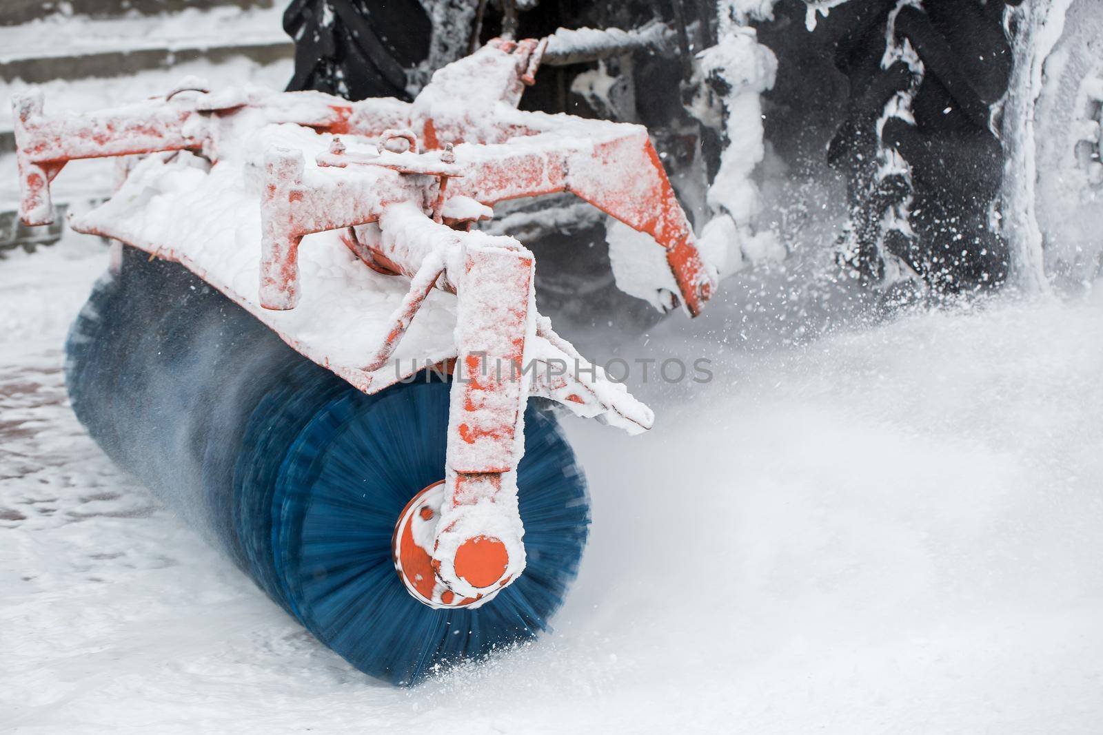 City service cleaning snow , a small tractor with a rotating brush clears a road in the city park from the fresh fallen snow on winter day