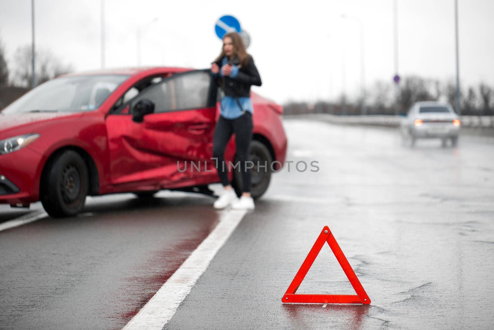 Driver sitting at roadside after traffic accident. Focus is on the red triangle sign