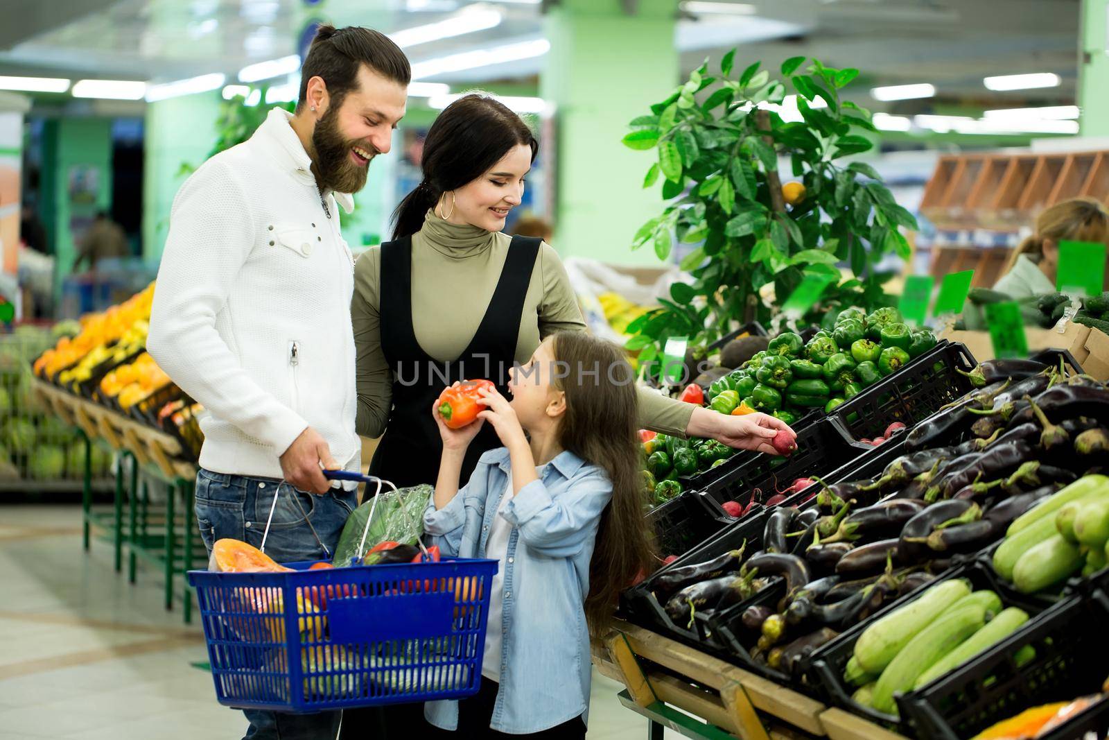 a woman with a man and a child, choosing vegetables while shopping in a vegetable supermarket. by StudioPeace