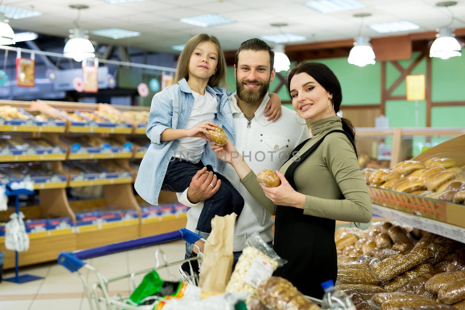 Beautiful young parents and their cute little daughter are smiling while choosing baking in the supermarket