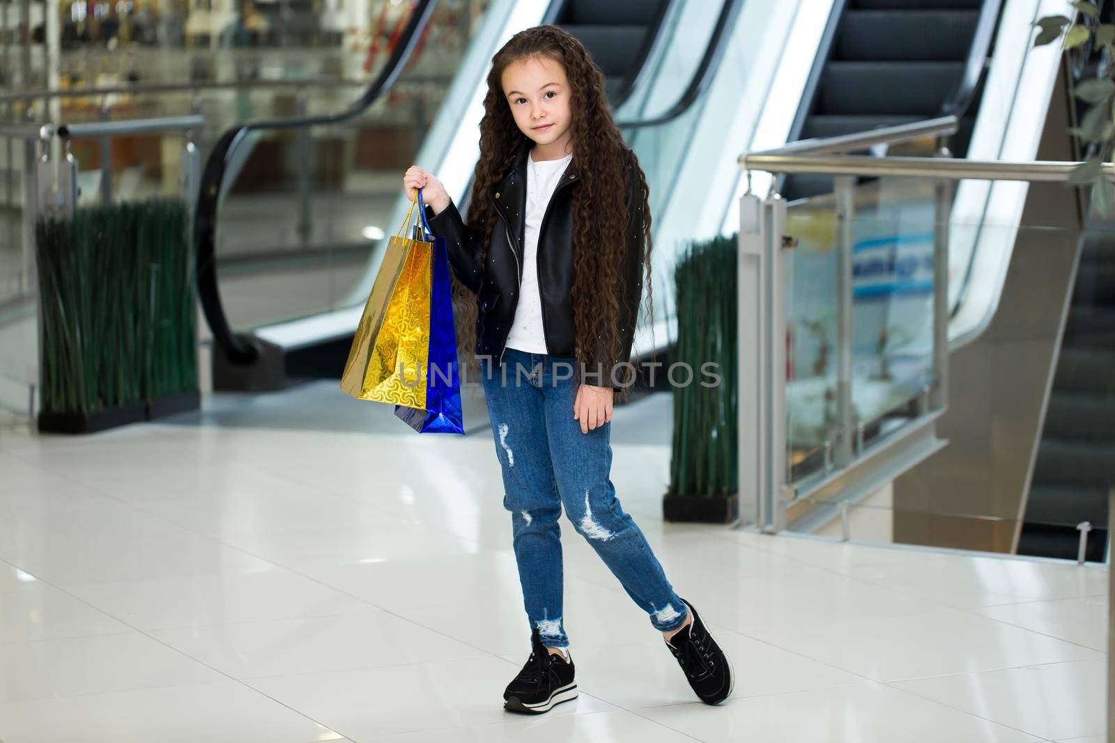 The happy child with color packages on the escalator, in shop of shopping center. by StudioPeace