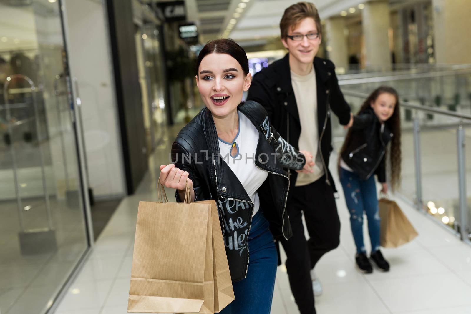 Happy young family with paper bags shopping at the Mall. Shop Windows with clothes. by StudioPeace