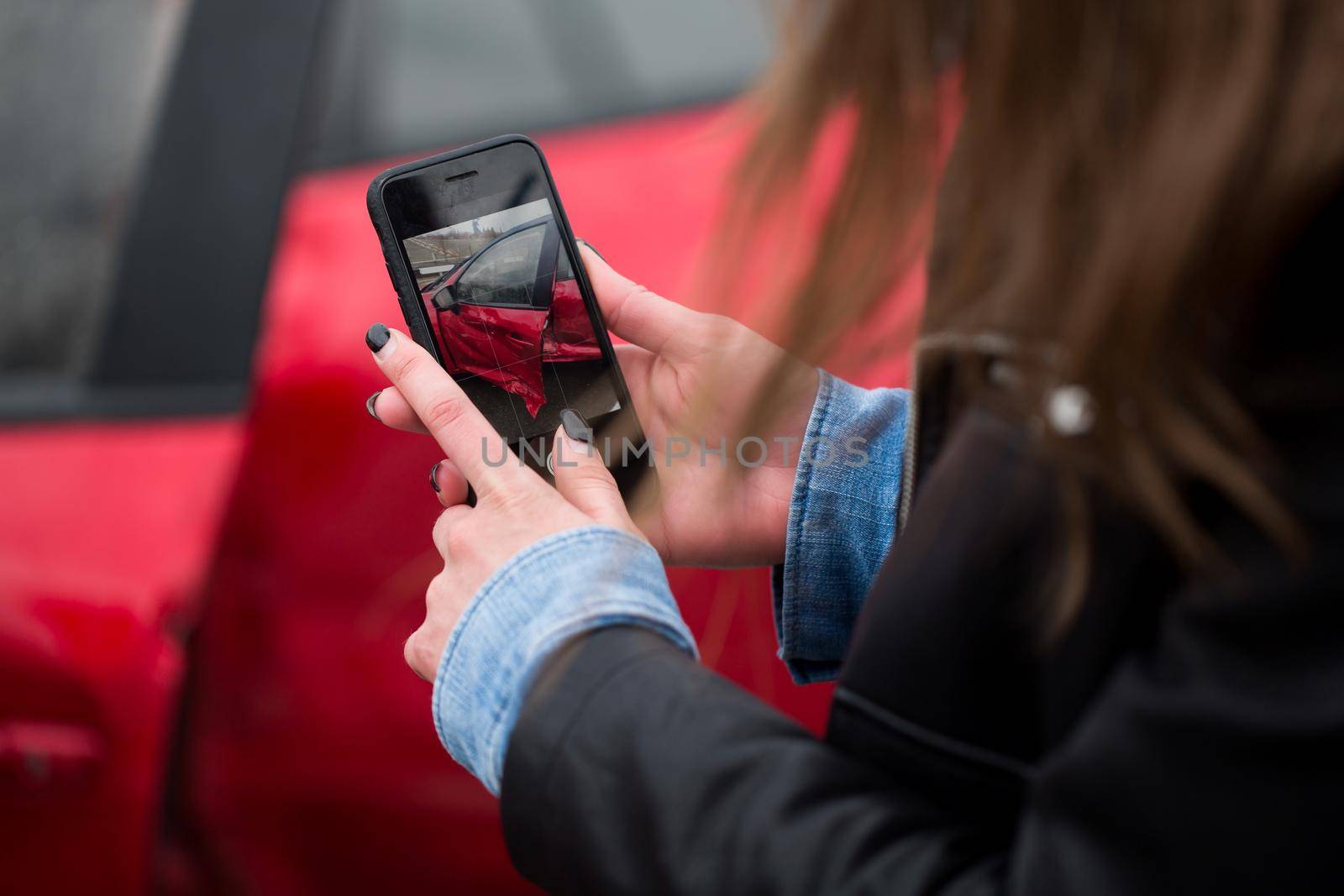 Woman using a smart phone to take a photo of the damage to her car caused by a car crash. by StudioPeace