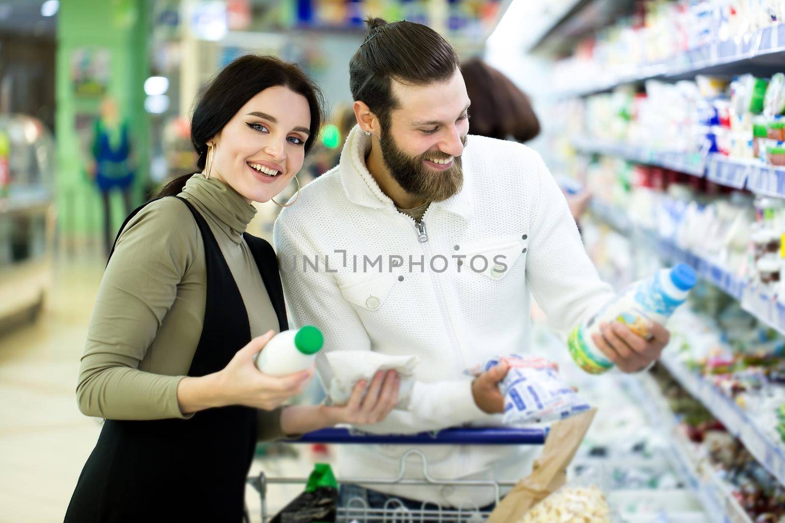A young family, a man and a woman choose milk in a large supermarket.