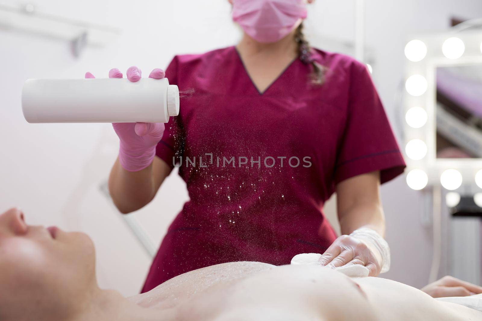 Cosmetologist sprinkles talcum or powdered breast of a muscular man before a hair removal procedure with sugar paste. Shugaring. Close-up