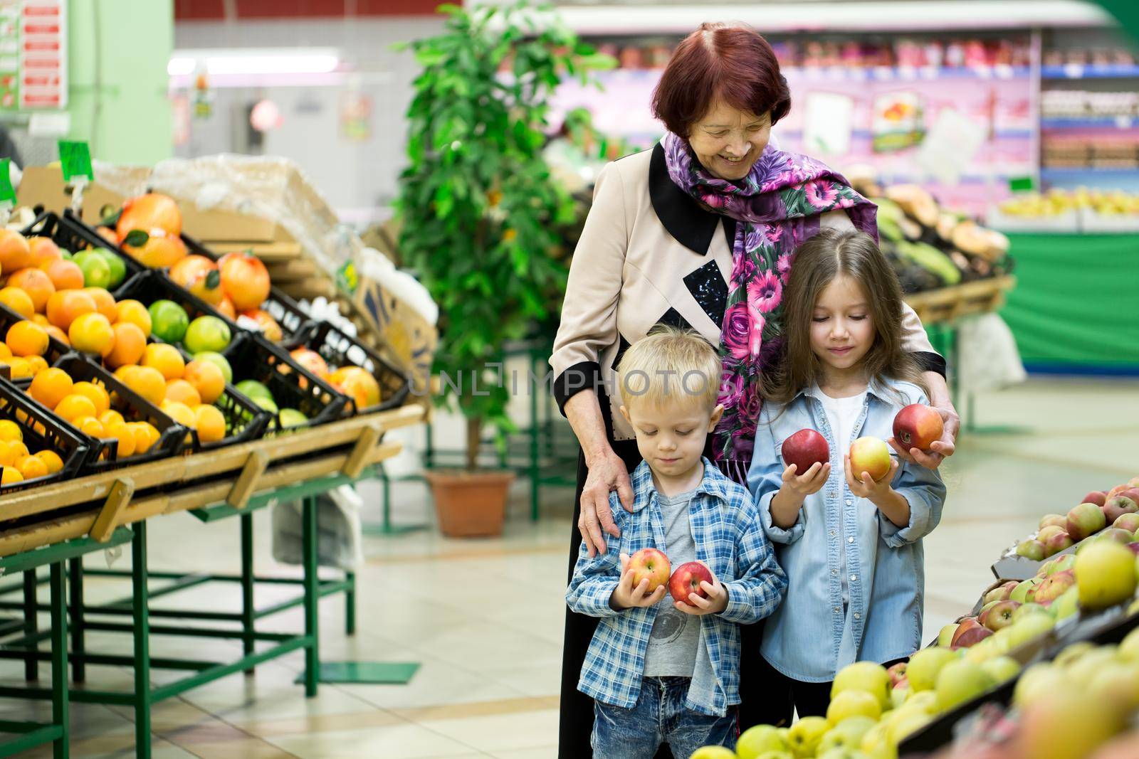 An old woman, a grandmother with grandchildren choose vegetables and fruits in a large supermarket by StudioPeace
