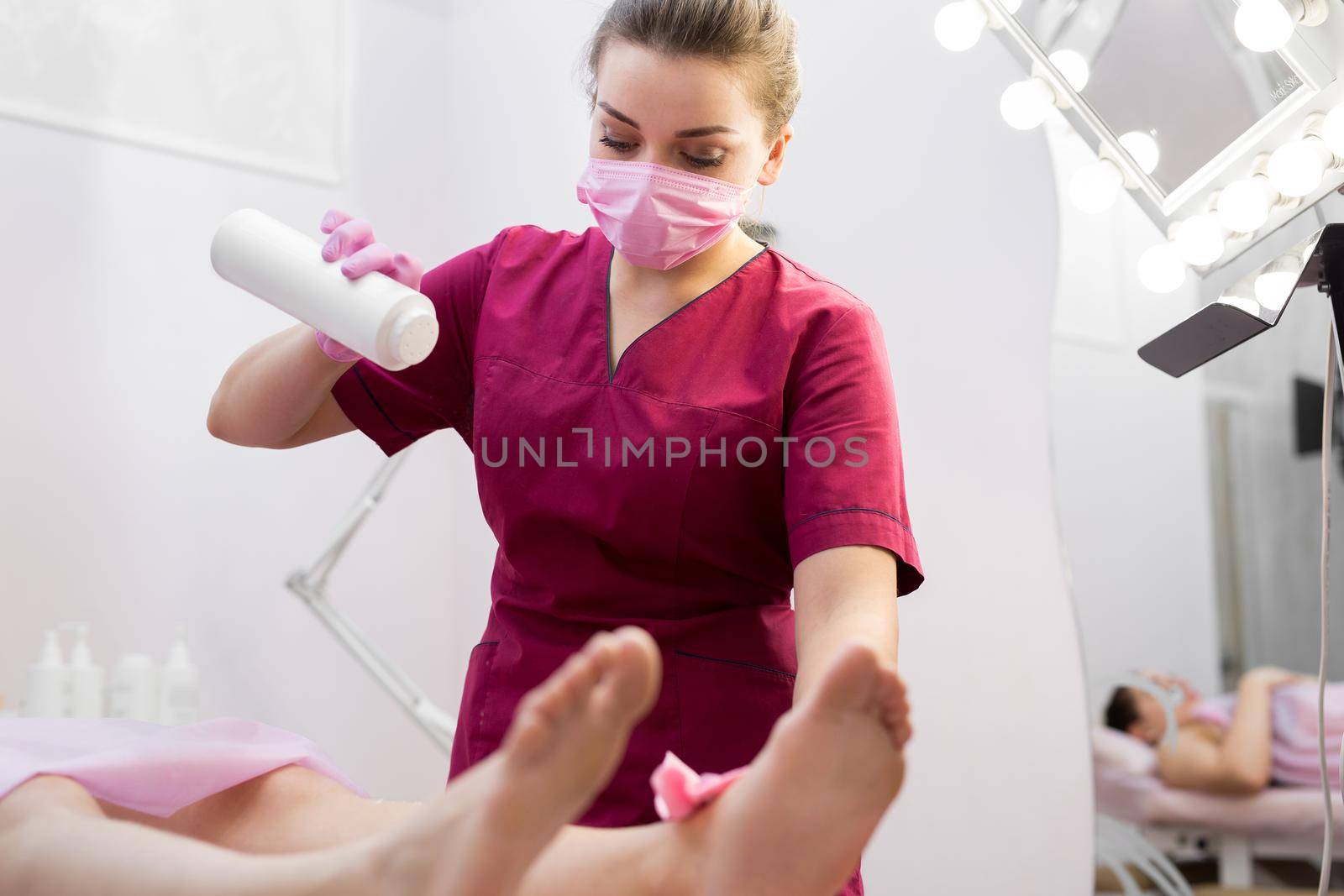 Cosmetologist sprinkles talcum powder on a young girl's leg before the depilation procedure. The girl lies on a couch in a beauty salon, she does the procedure shugaring. by StudioPeace
