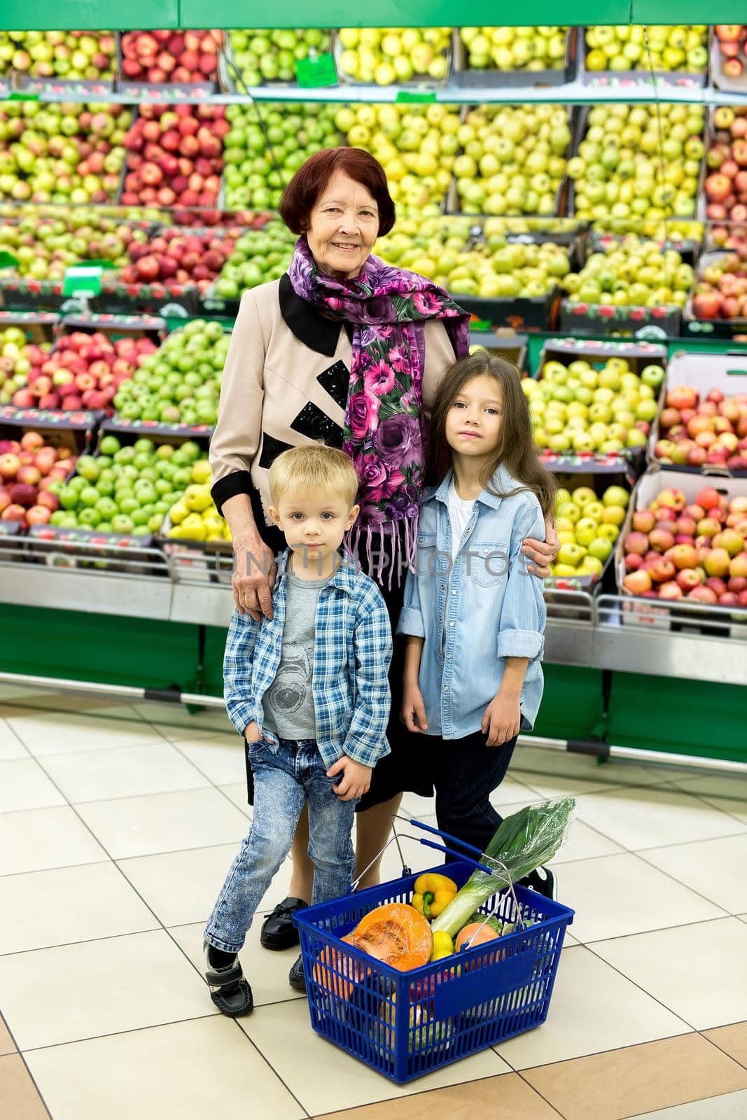 An old woman, a grandmother with grandchildren choose vegetables and fruits in a large supermarket.