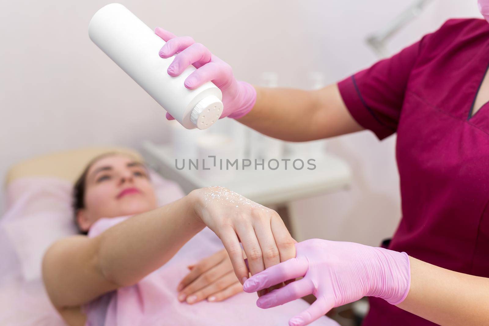 Close-up of a beautician sprinkles talcum powder on a young girl's hand before the depilation procedure. The girl lies on a couch in a beauty salon, she does the procedure shugaring