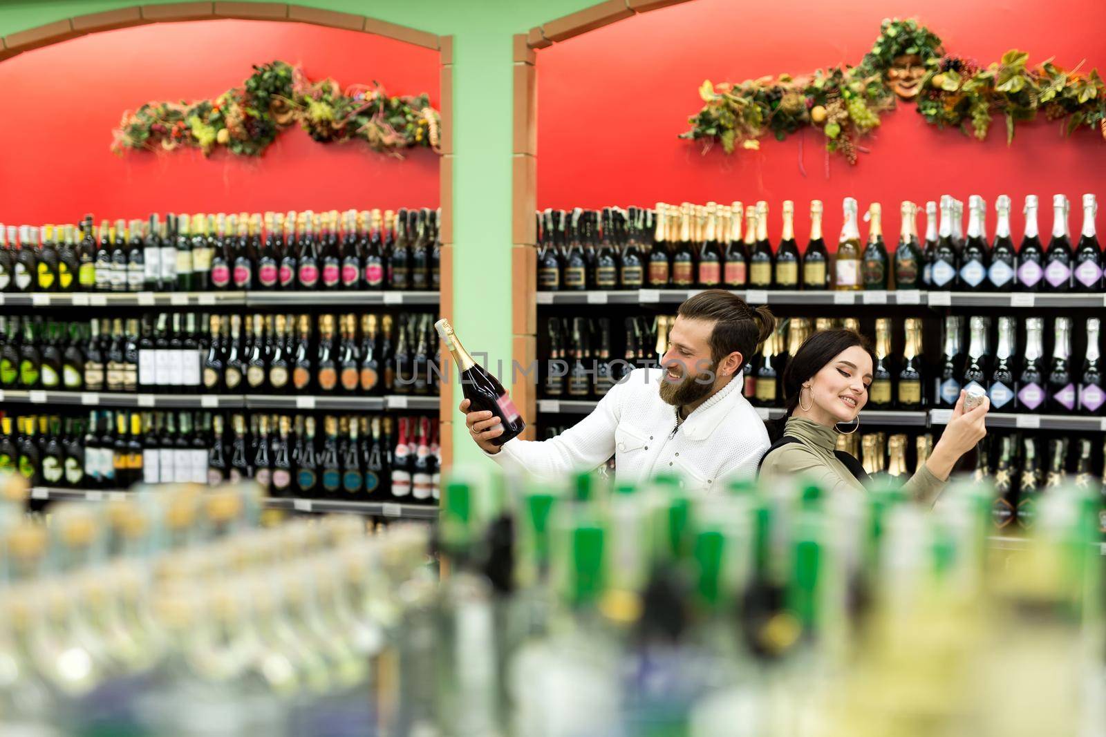 A young family, a man and a woman choose alcohol in a large supermarket by StudioPeace