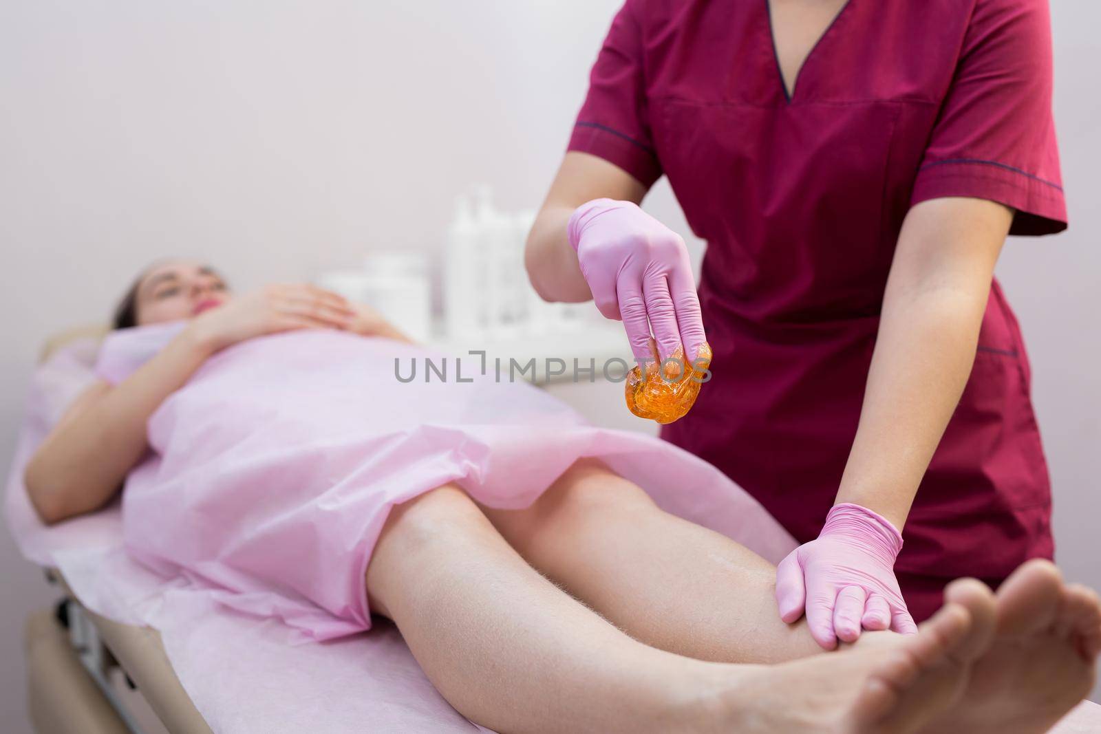 Sugar depilation of the feet in the beauty salon. Rid of hair on the legs. Sugaring. Master shugaring applies thick sugar paste on the legs of a young girl, removing hair on the legs. Close-up by StudioPeace