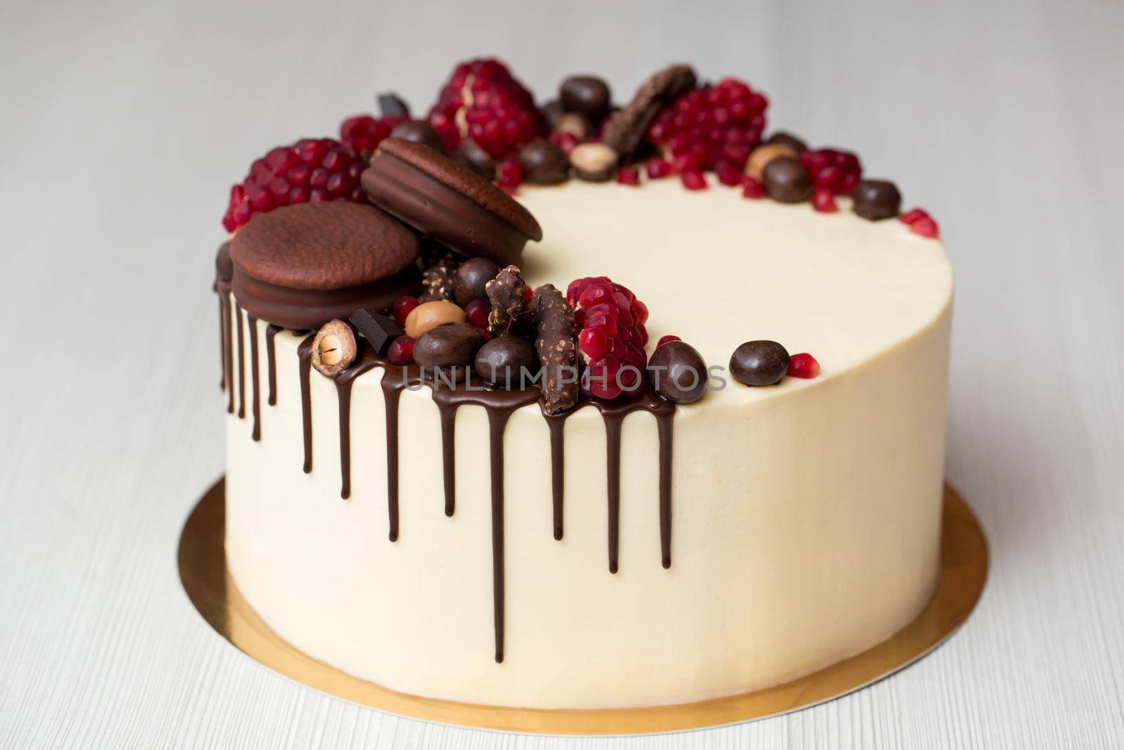 cake with white cream, chocolate drips, pomegranate, nuts and chocolate decor. by StudioPeace