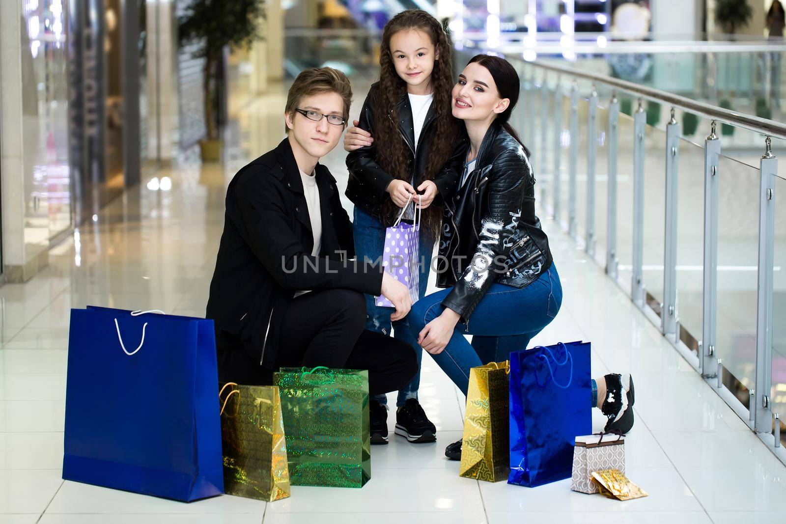 Happy young family with paper bags shopping at the Mall. Shop Windows with clothes. by StudioPeace