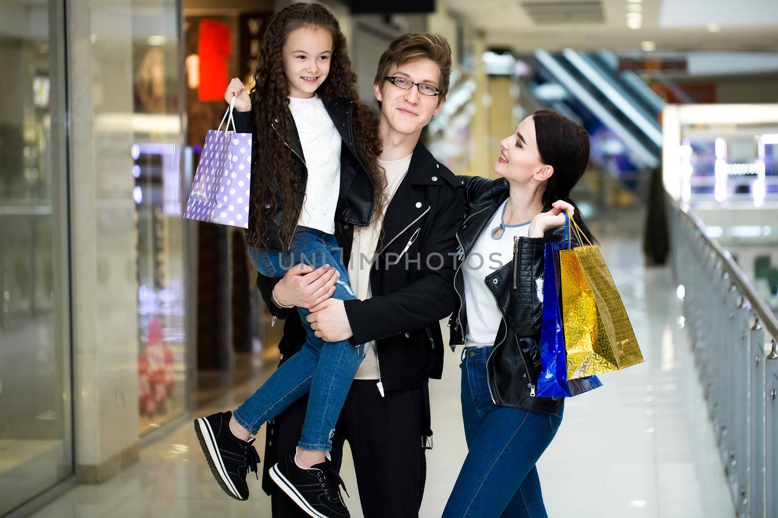 Happy young family with paper bags shopping at the Mall. Shop Windows with clothes. by StudioPeace