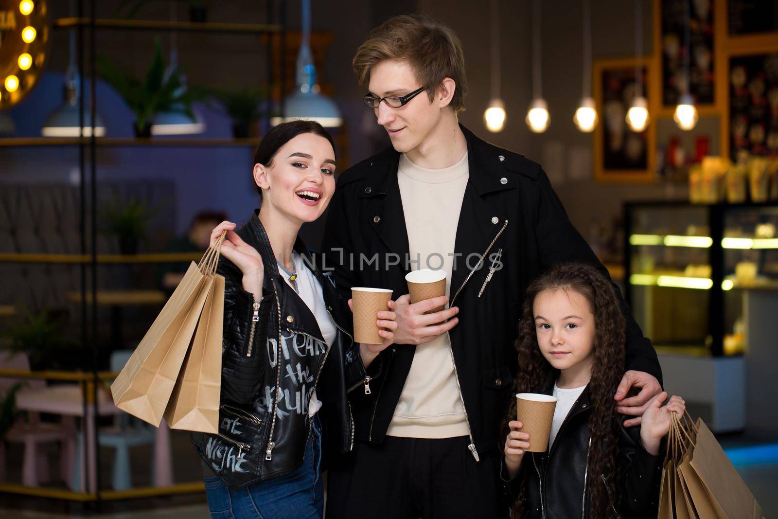 Young family having time in a cafe after shopping. Mom, dad, little daughter drink tea and cafe. Family having time in a cafe after shopping. by StudioPeace