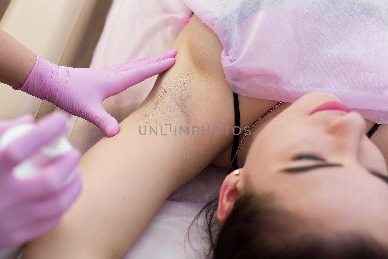 Close-up of armpit of a young girl with hair, hair removal procedure in a beauty salon. Beautician makes shugaring underarms for a young woman. Depilation of armpit with sugar paste. by StudioPeace