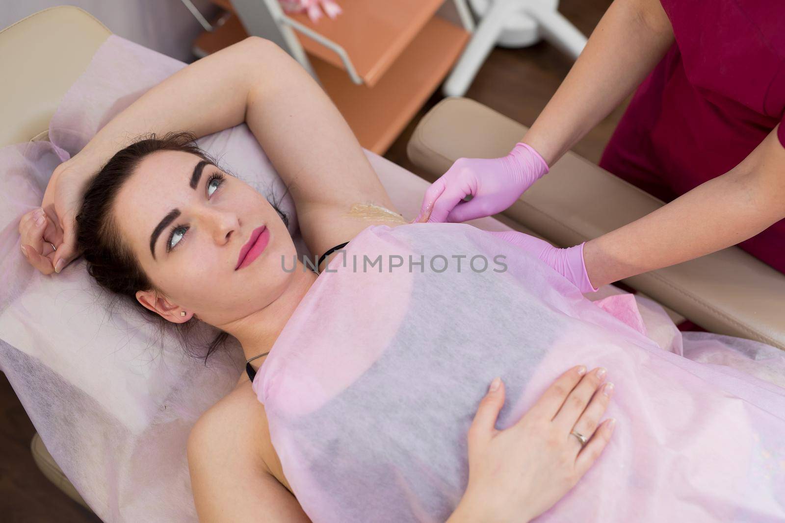 master of sugaring puts paste on the girl's armpits. Professional woman at spa beauty salon doing epilation armpits using sugar. Sugaring