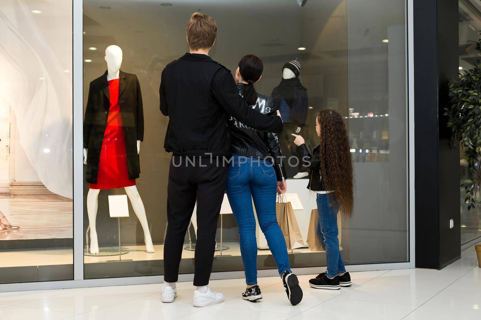 Happy young family with paper bags shopping at the Mall. Shop Windows with clothes. by StudioPeace