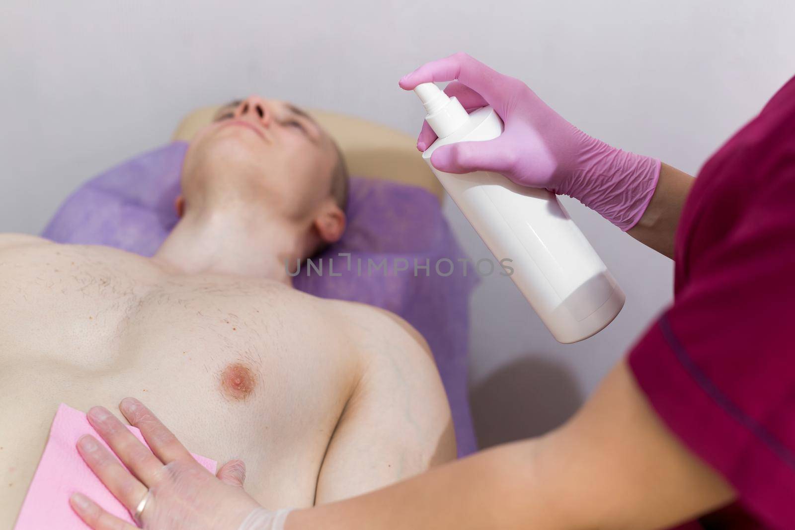 Close-up of mens Breasts in the beauty salon for the procedure of sugar hair removal. Beautician sprays disinfectant solution on the man's chest. Sugaring. by StudioPeace