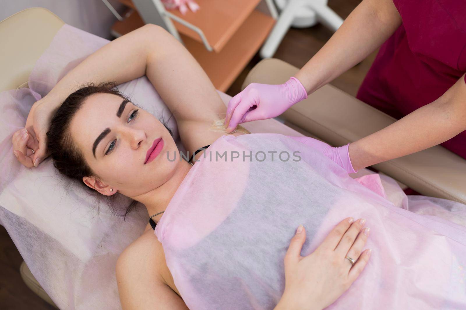 master of sugaring puts paste on the girl's armpits. Professional woman at spa beauty salon doing epilation armpits using sugar. Sugaring