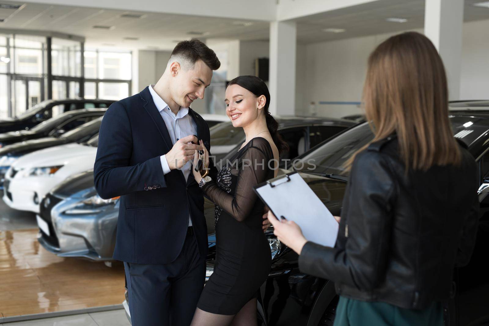 A couple of men and women are happy to buy a new car in a car dealership with the seller.