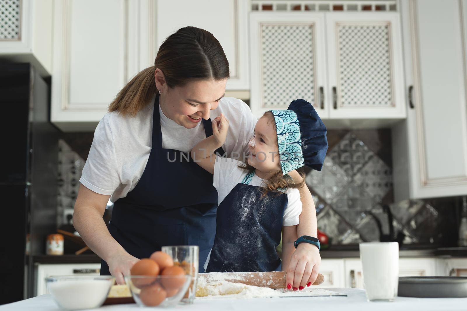 Mother and daughter in matching aprons and chef's hat cooking in the kitchen. They roll out the dough and sprinkle it with flour by StudioPeace