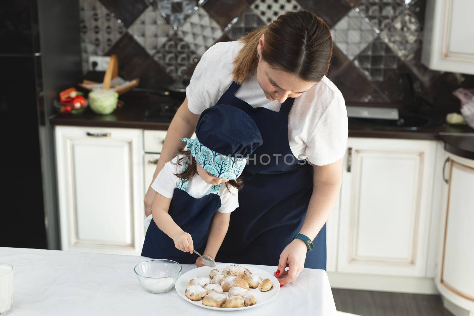 Mom and daughter in the kitchen sprinkle cookies with powdered sugar by StudioPeace