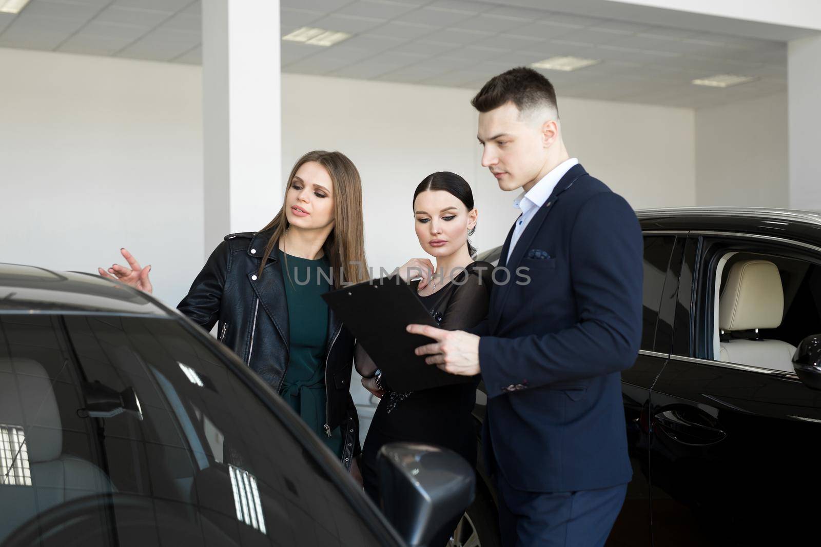 Auto business, car sales - a couple of friends of girls with a car dealer choose a car in a car dealership. by StudioPeace
