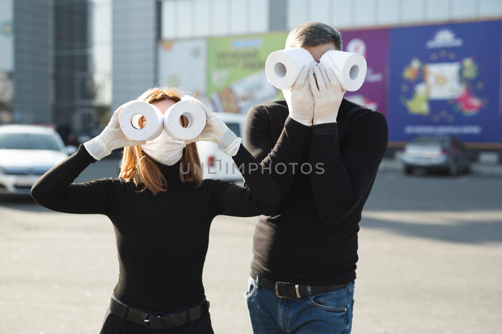 Woman and a man in a coronavirus face mask hold large rolls of toilet paper on a city street and indulge