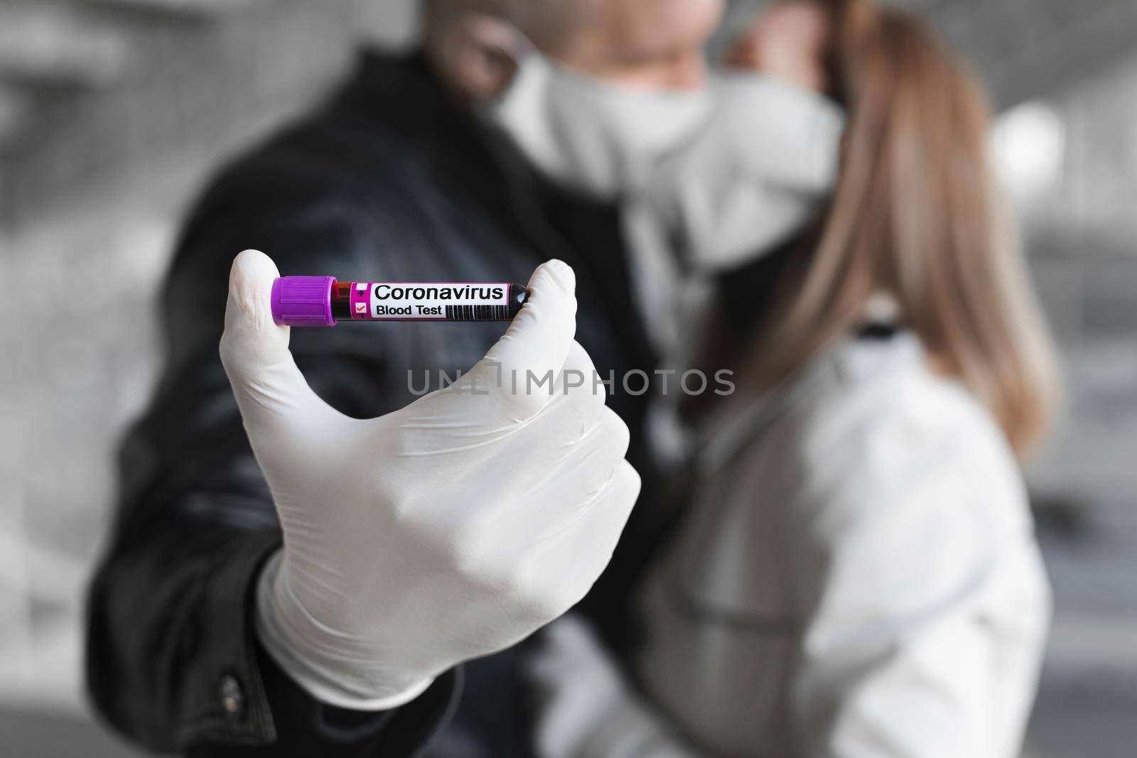 Man's hands holding a test tube with a blood sample for research new rapidly spreading Coronavirus Covid-19. A man and a woman kiss in a medical mask
