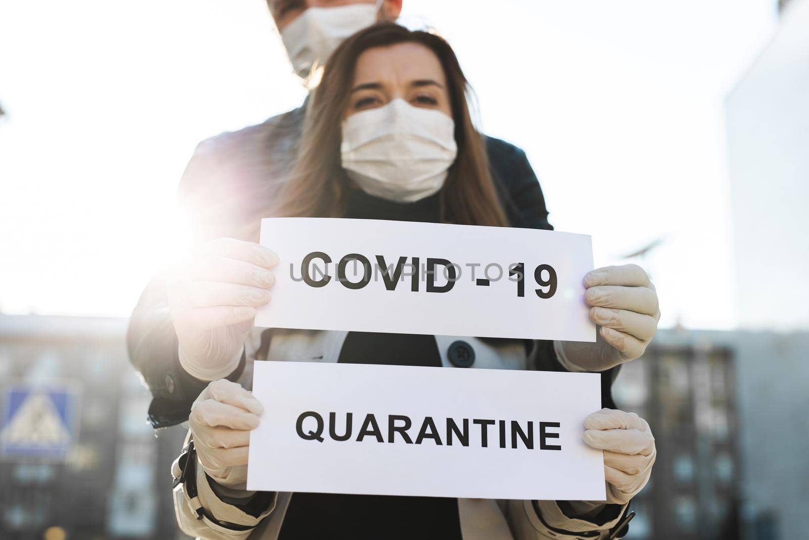 A woman and a man in protective medical masks hold a placard with the words Quarantine and Covid 19.