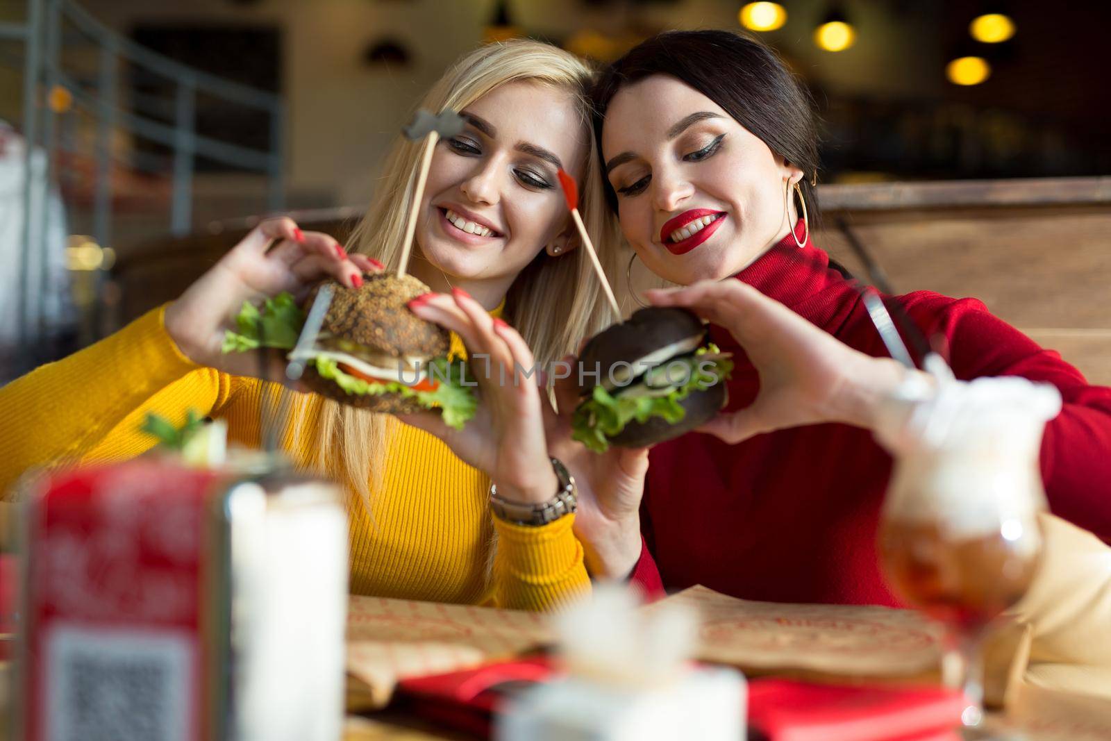 Two happy girls bite burgers. Concept of fast food. by StudioPeace