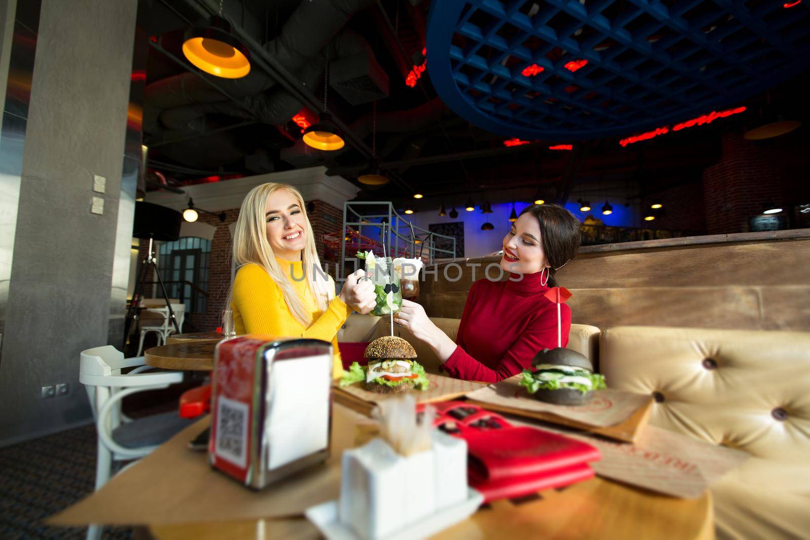 Young women toasting cocktail glasses in a cafe. by StudioPeace