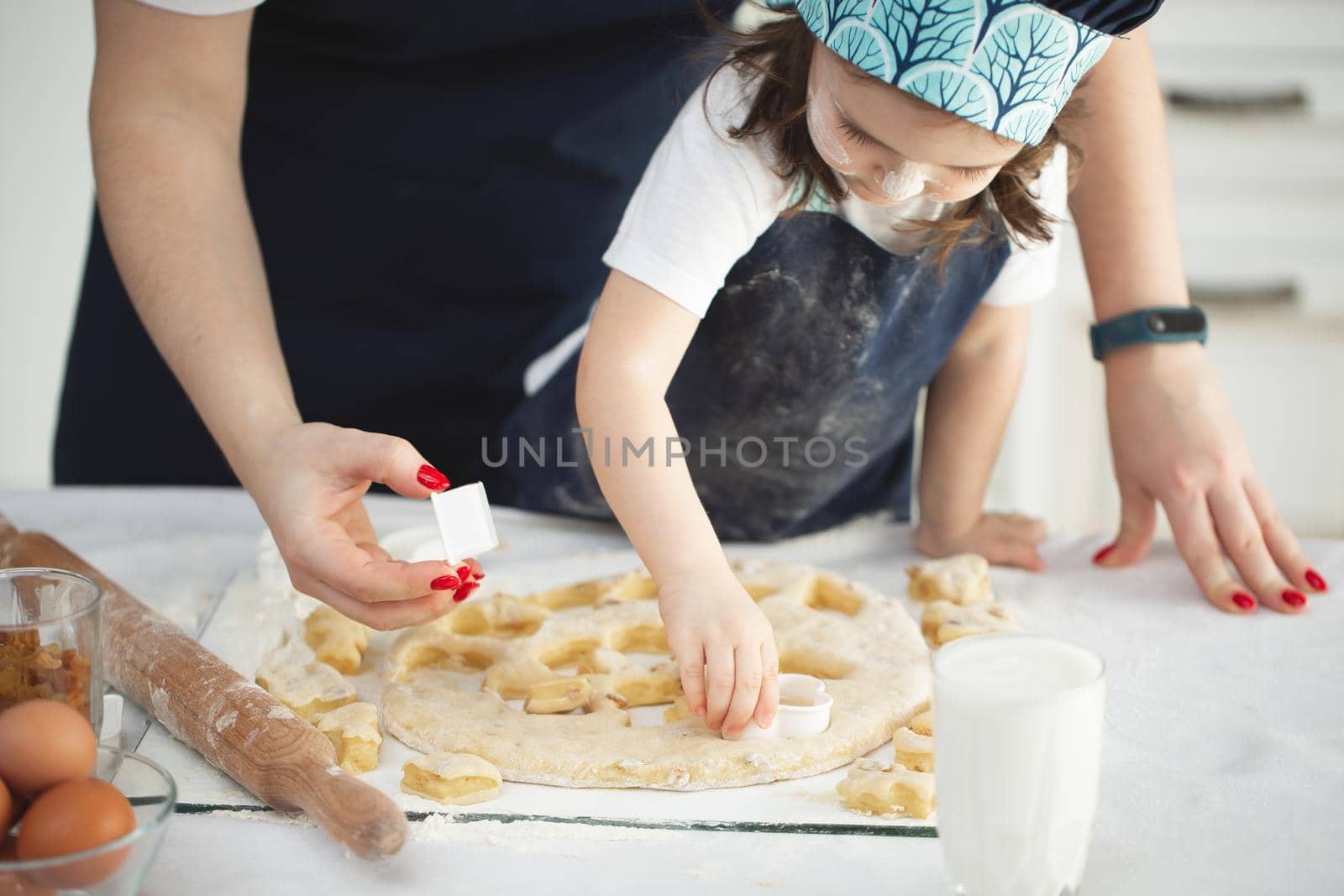Mother and her little daughter preparing pastry in the kitchen. Little girl using metallic form to cut the dough. by StudioPeace