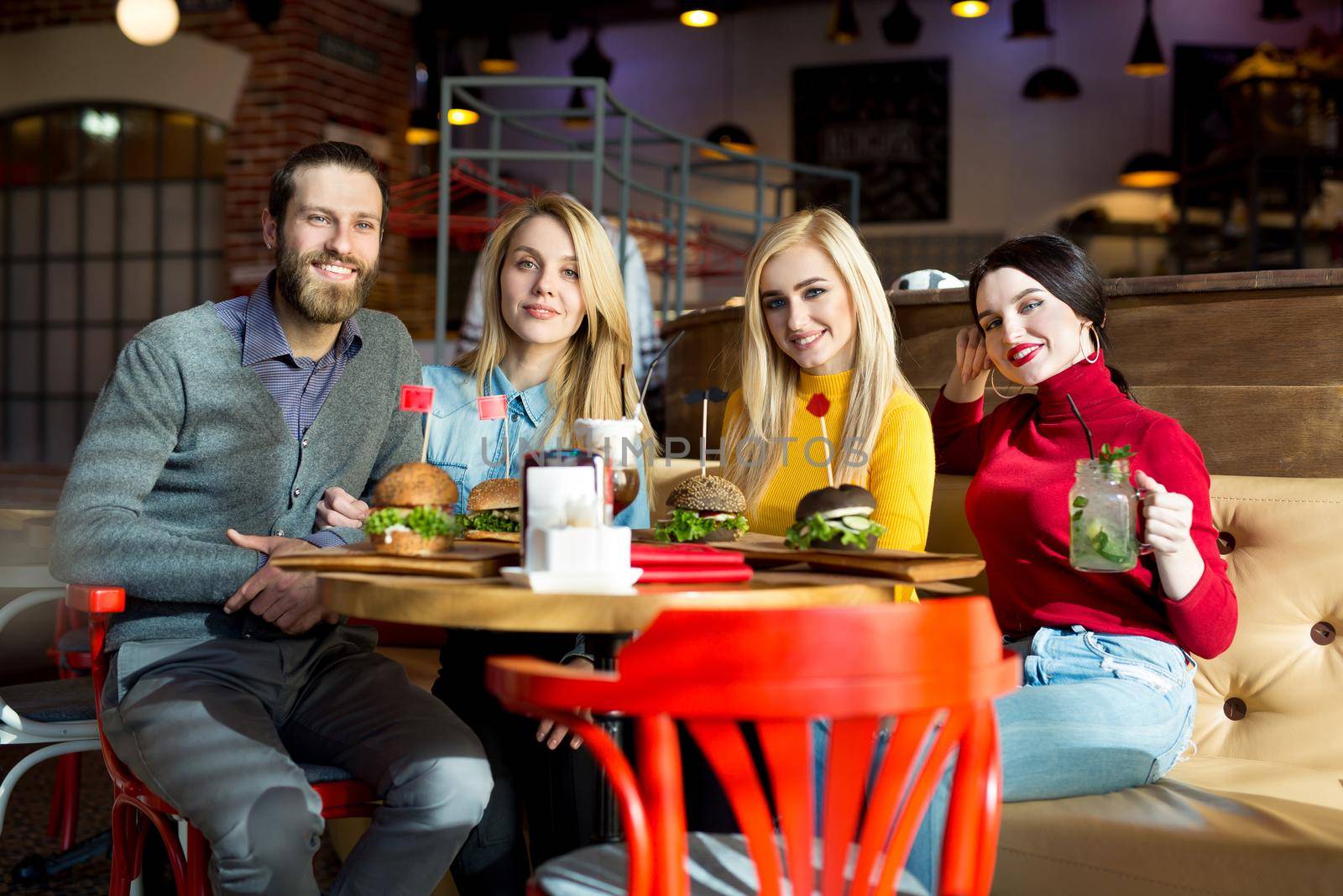 People have dinner together at a table in a cafe. Happy friends eat burgers and drink cocktails in the restaurant.