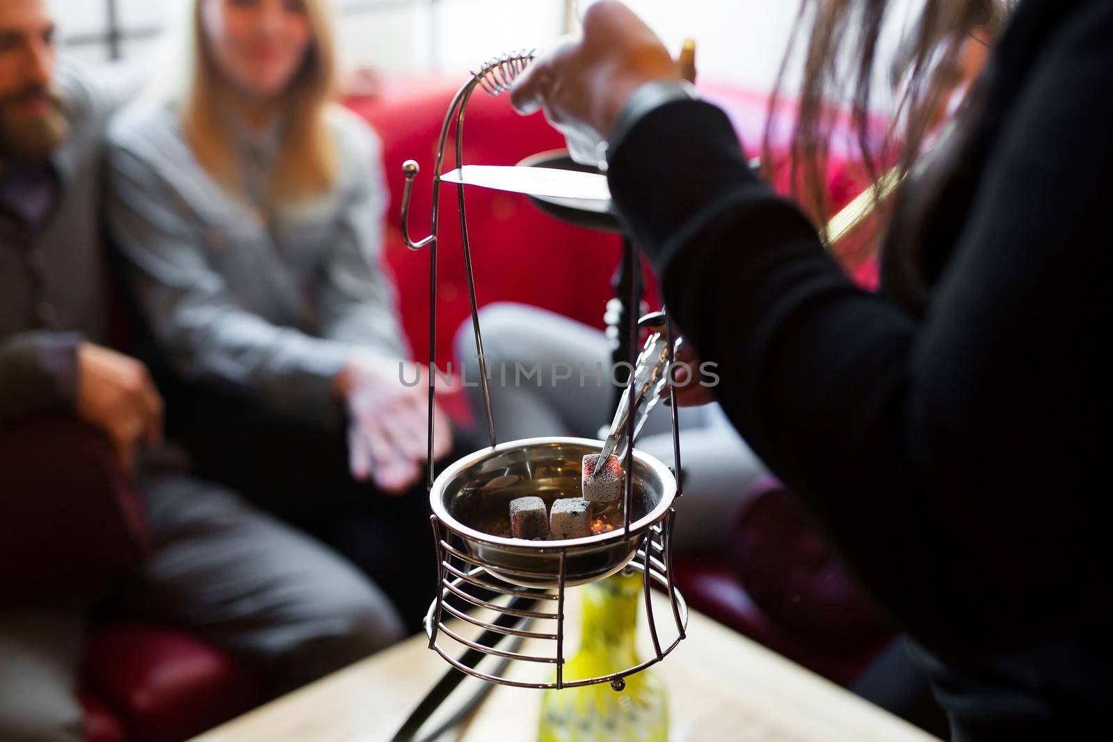 The girl puts hot coals in the hookah with tongs by StudioPeace