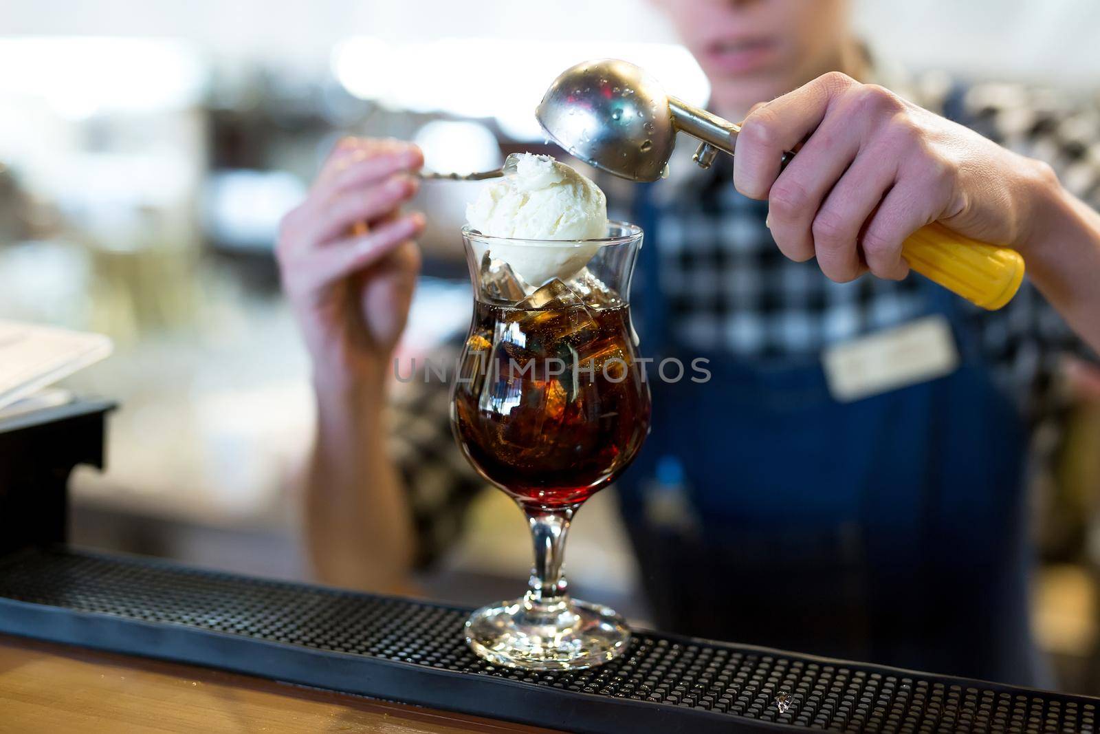 The bartender in the restaurant puts a ball of ice cream in a glass with a cocktail.
