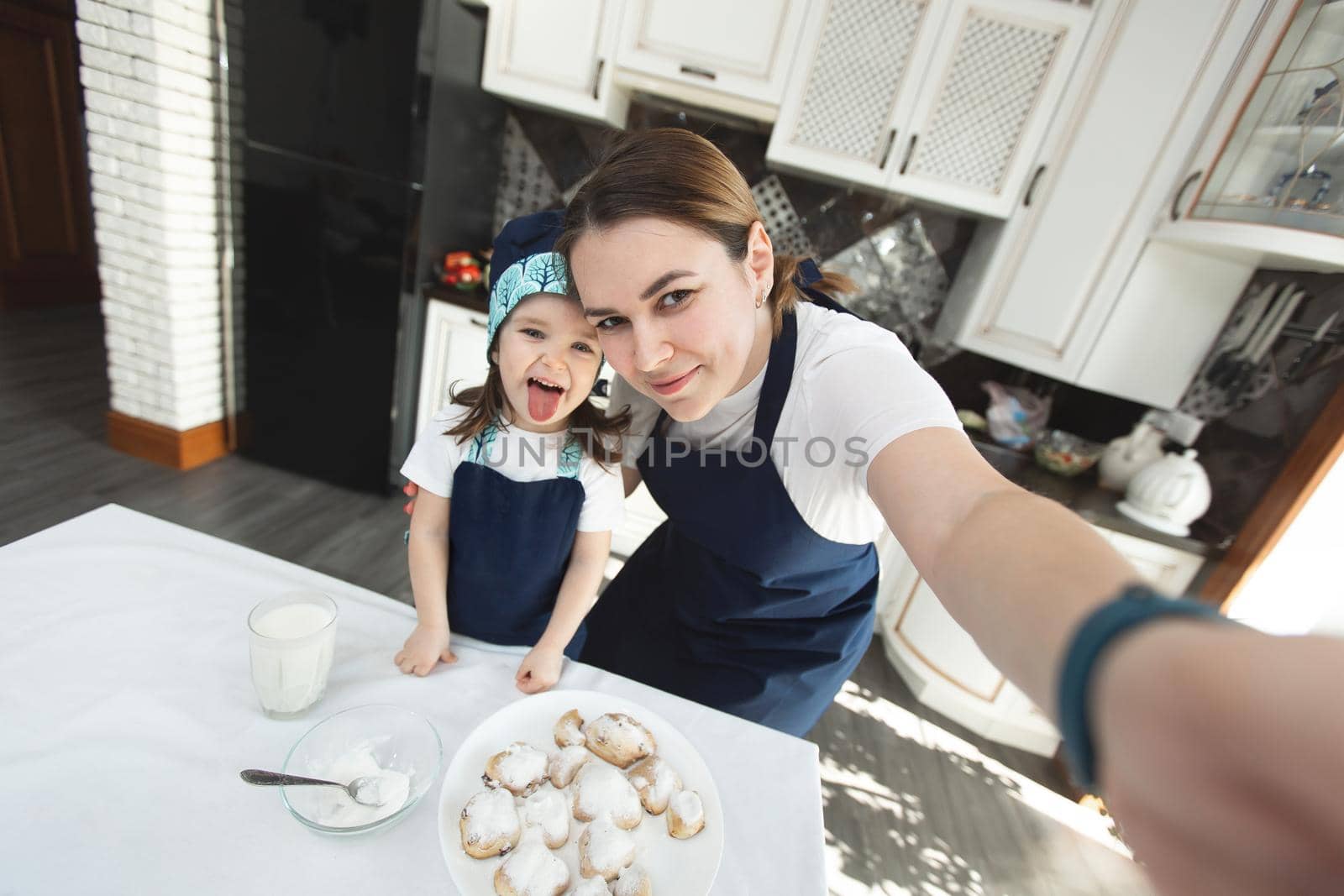 Mom and her daughter bake cookies at home in the modern kitchen and making selfie. by StudioPeace