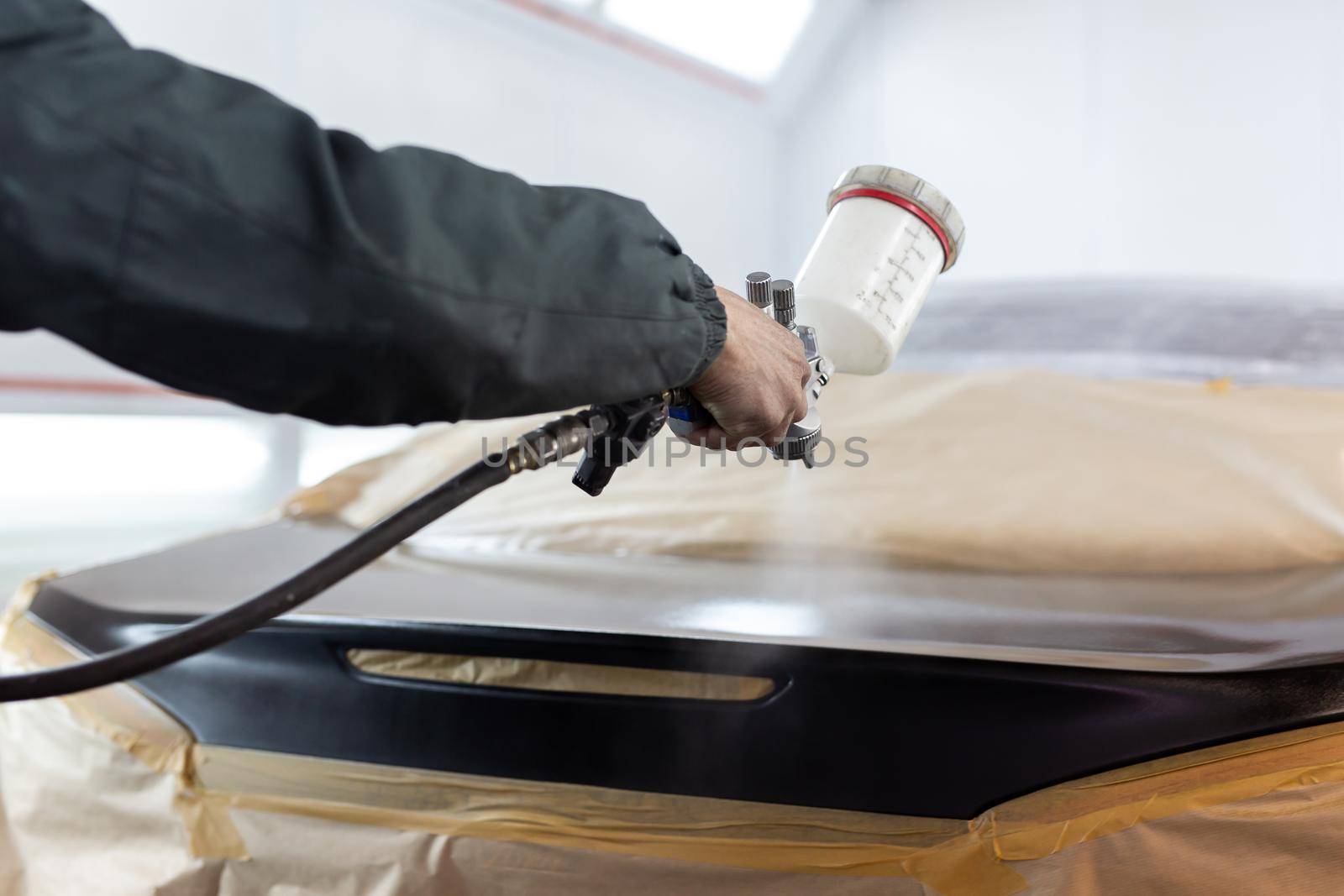 Close-up of a spray gun with black paint for painting a car in a special booth by StudioPeace