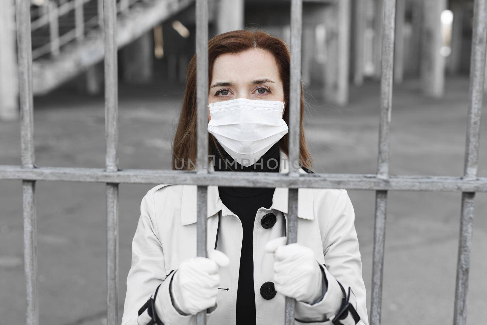 Girl in the medical mask is in the street in isolation and is holding fence. Coronavirus. Covid19. by StudioPeace